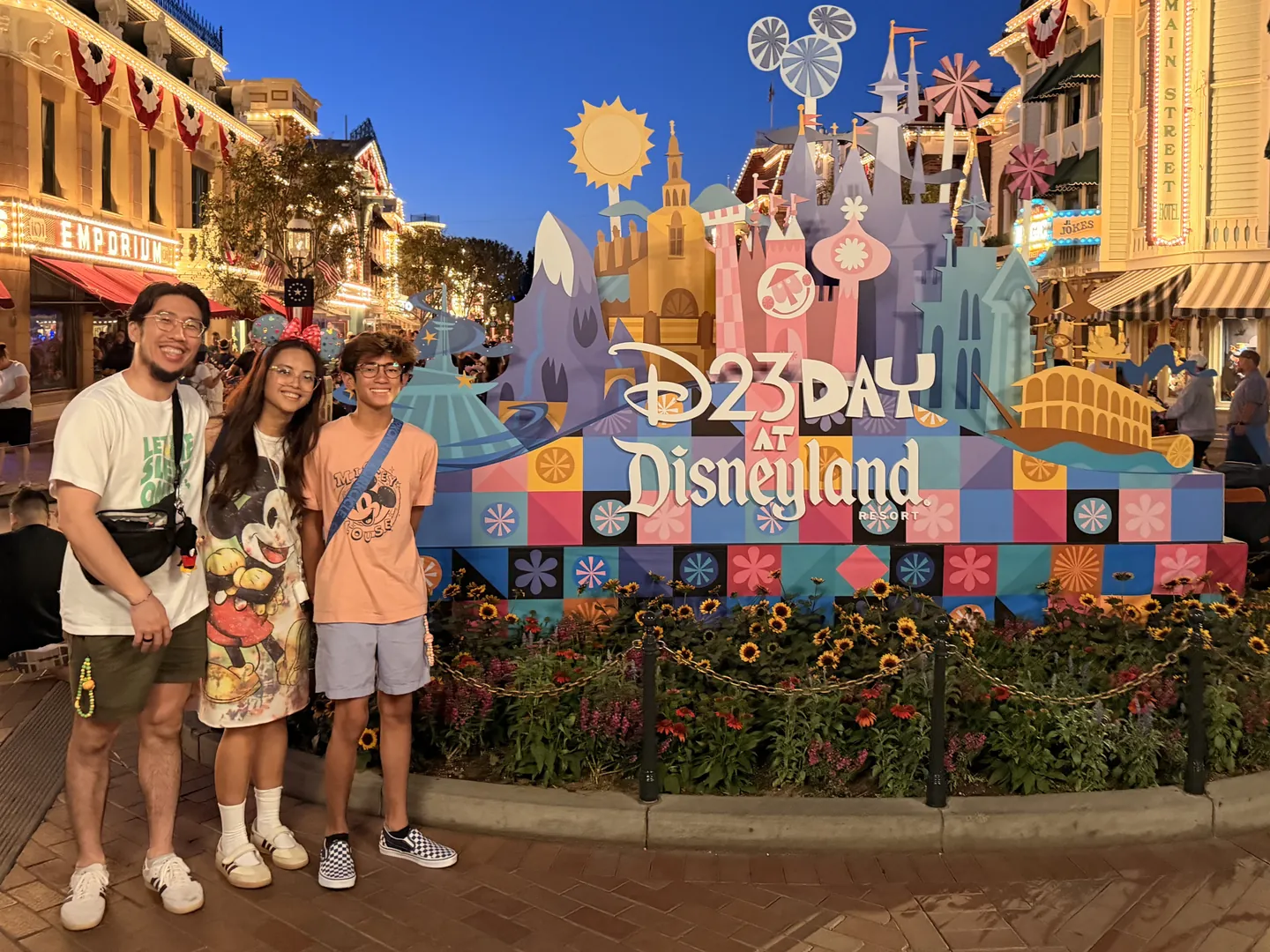 Phil and family on Main Street, U.S.A. at Disneyland at dusk, beside a colorful D23 Day display
