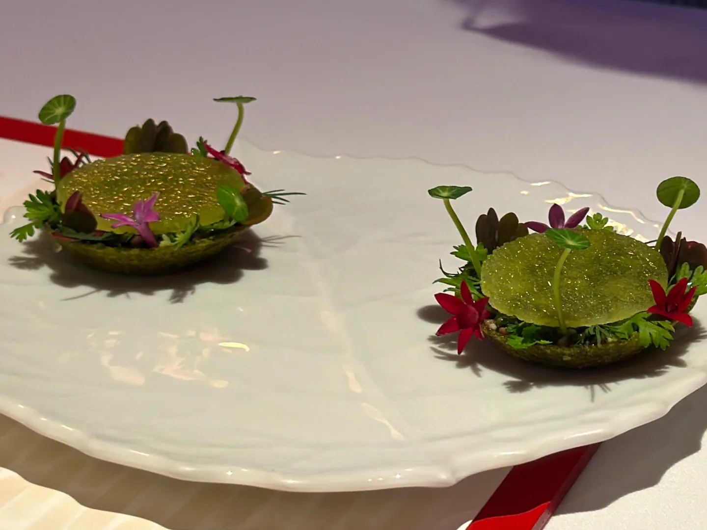 Two small green tarts topped with sprouts and edible flowers on a white plate, a course at a tasting-menu dinner